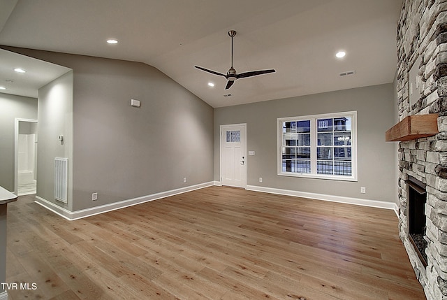 unfurnished living room featuring lofted ceiling, a stone fireplace, light hardwood / wood-style flooring, and ceiling fan