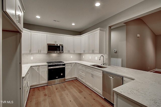 kitchen featuring sink, appliances with stainless steel finishes, white cabinetry, backsplash, and light hardwood / wood-style floors