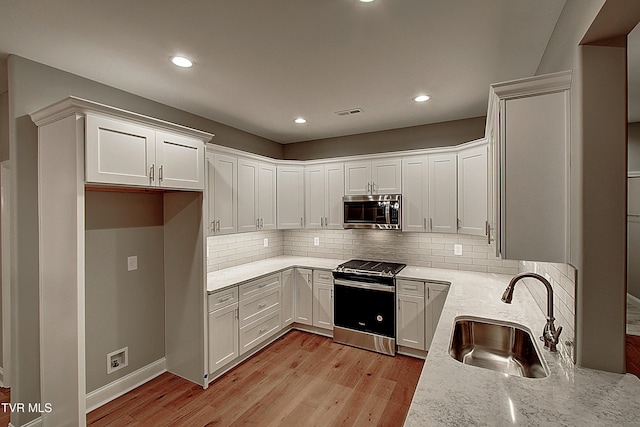 kitchen featuring sink, white cabinetry, appliances with stainless steel finishes, light stone countertops, and light hardwood / wood-style floors