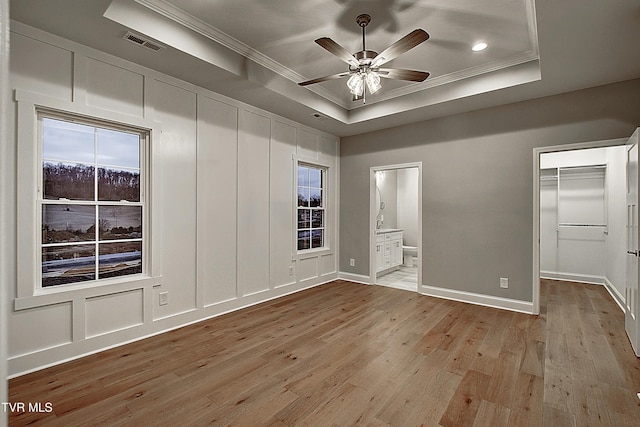 unfurnished bedroom with ensuite bathroom, light hardwood / wood-style floors, ornamental molding, a spacious closet, and a raised ceiling