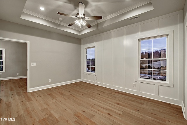 empty room with a tray ceiling, ornamental molding, ceiling fan, and light wood-type flooring