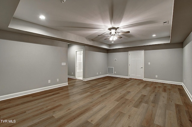 empty room featuring a tray ceiling, ceiling fan, and light wood-type flooring