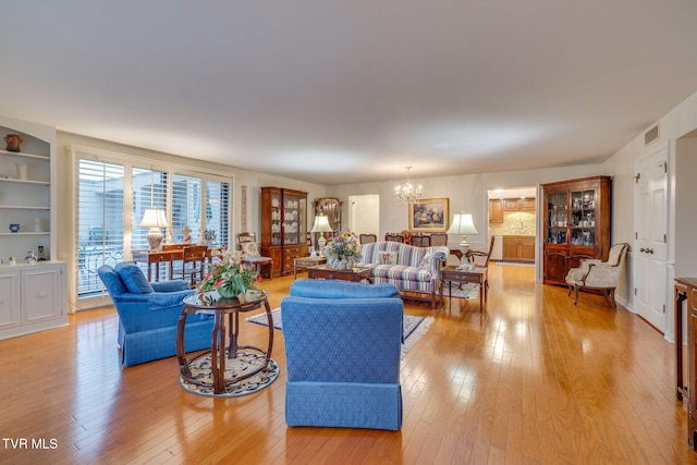 living room with built in features, light wood-type flooring, and a notable chandelier