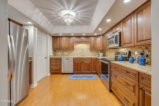 kitchen with sink, light stone counters, light hardwood / wood-style flooring, a chandelier, and appliances with stainless steel finishes