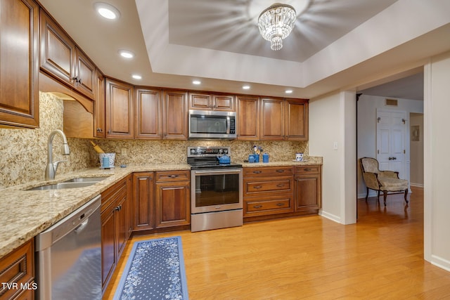 kitchen featuring backsplash, an inviting chandelier, sink, appliances with stainless steel finishes, and a tray ceiling