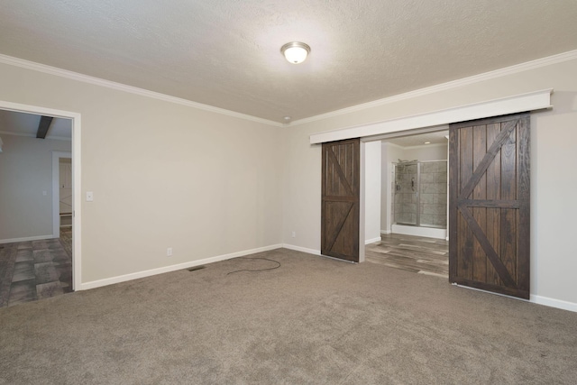 unfurnished bedroom with a barn door, a textured ceiling, dark carpet, and ensuite bath