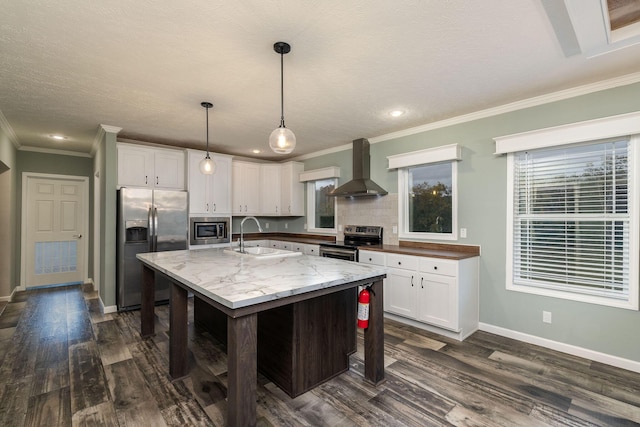 kitchen featuring white cabinetry, sink, hanging light fixtures, wall chimney range hood, and appliances with stainless steel finishes