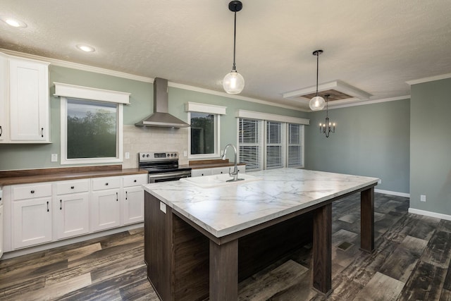 kitchen with white cabinetry, electric range, wall chimney exhaust hood, hanging light fixtures, and a center island with sink