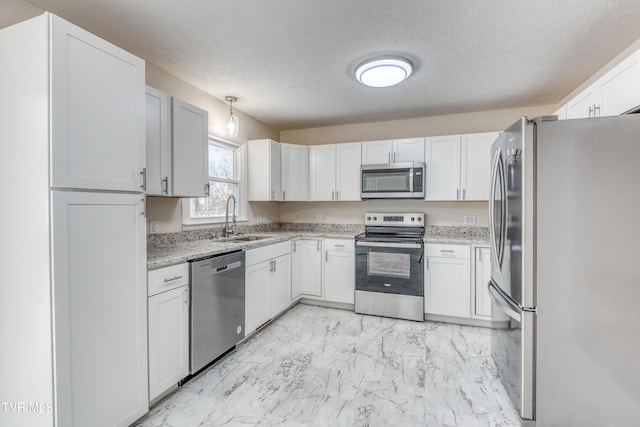 kitchen with light stone counters, stainless steel appliances, sink, decorative light fixtures, and white cabinets