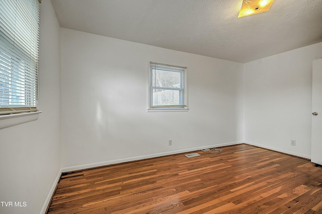 empty room with a textured ceiling, dark hardwood / wood-style flooring, and plenty of natural light