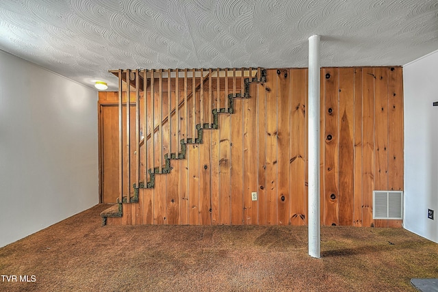 basement featuring carpet, wood walls, and a textured ceiling