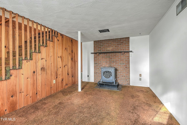 unfurnished living room with a wood stove, wood walls, carpet, and a textured ceiling