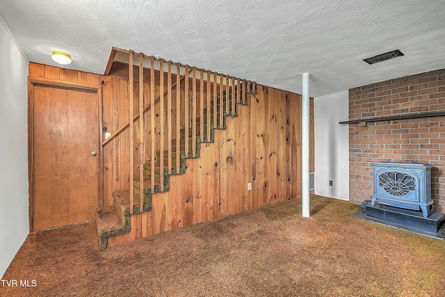 basement featuring a textured ceiling, carpet floors, a wood stove, and wood walls