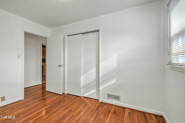 unfurnished bedroom with a textured ceiling, hardwood / wood-style flooring, and a closet