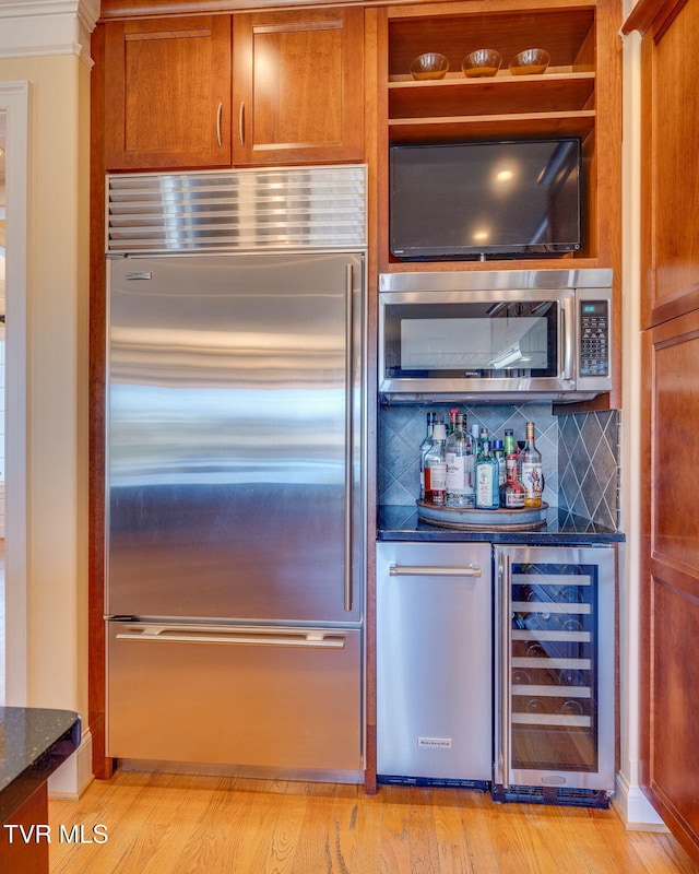 kitchen featuring stainless steel appliances, wine cooler, light hardwood / wood-style flooring, backsplash, and dark stone counters