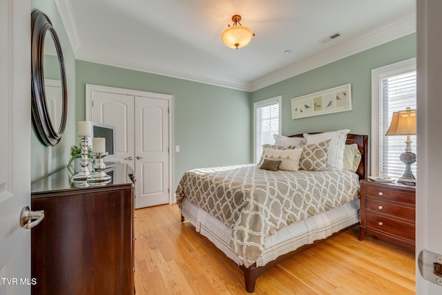 bedroom featuring a closet, light hardwood / wood-style flooring, multiple windows, and crown molding