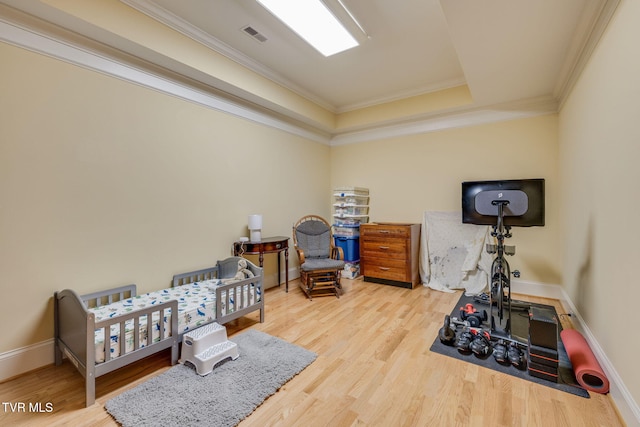 bedroom with a raised ceiling, crown molding, a nursery area, and hardwood / wood-style flooring