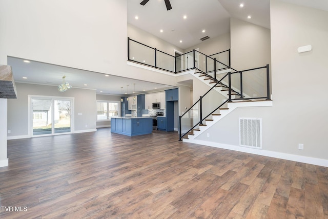 unfurnished living room with ceiling fan, a towering ceiling, and dark hardwood / wood-style floors