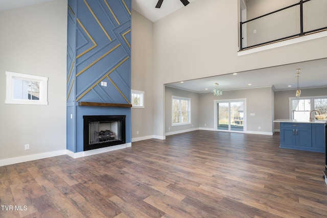 unfurnished living room featuring ceiling fan, a large fireplace, dark hardwood / wood-style floors, and crown molding