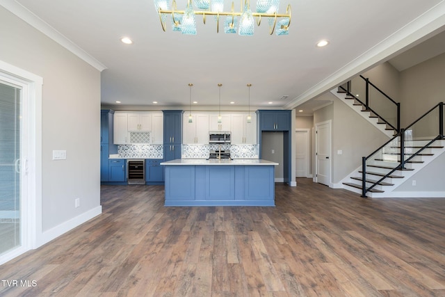 kitchen featuring a center island with sink, pendant lighting, crown molding, stainless steel appliances, and beverage cooler