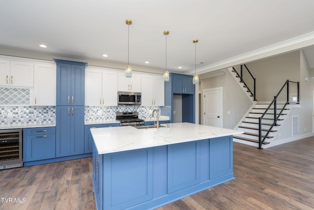 kitchen with sink, hanging light fixtures, appliances with stainless steel finishes, an island with sink, and beverage cooler