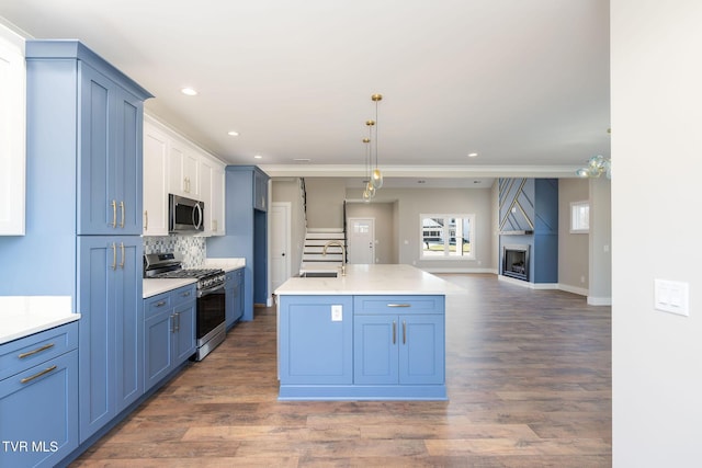 kitchen featuring decorative light fixtures, backsplash, sink, a kitchen island with sink, and appliances with stainless steel finishes