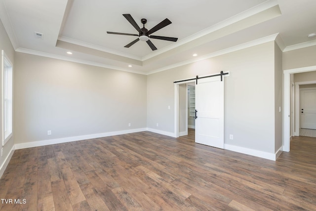 interior space with ceiling fan, a barn door, a tray ceiling, dark wood-type flooring, and ornamental molding