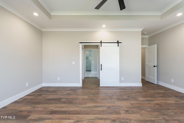 unfurnished bedroom with a barn door, ceiling fan, a raised ceiling, dark hardwood / wood-style floors, and ornamental molding