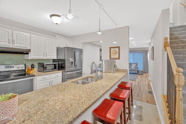 kitchen with white cabinetry, sink, hanging light fixtures, stainless steel appliances, and light stone counters