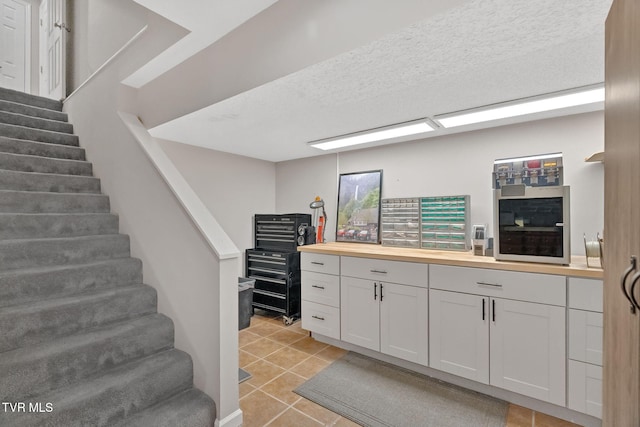 interior space with white cabinets, butcher block countertops, light tile patterned floors, and a textured ceiling