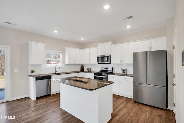 kitchen with appliances with stainless steel finishes, a center island, white cabinetry, and dark stone counters