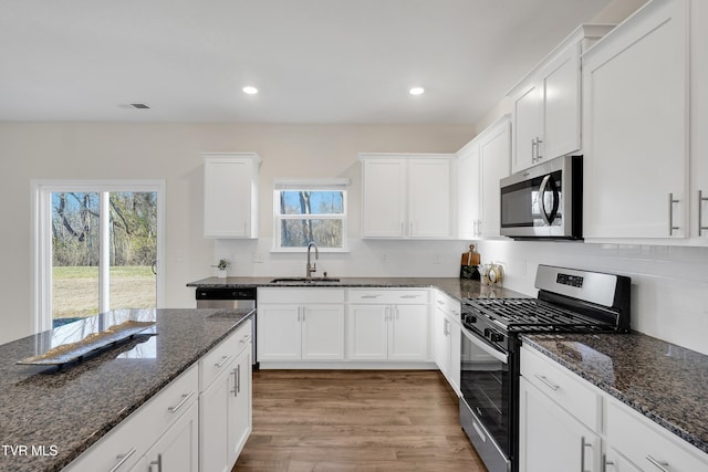 kitchen featuring white cabinets, stainless steel appliances, dark stone counters, and sink