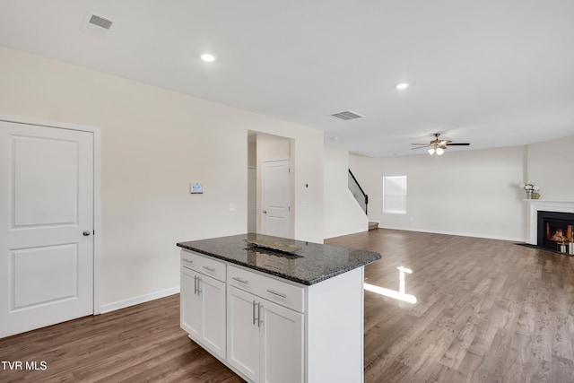 kitchen featuring ceiling fan, white cabinets, dark stone counters, wood-type flooring, and a kitchen island