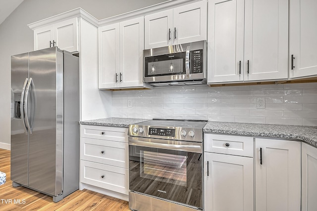 kitchen featuring white cabinets, decorative backsplash, light stone countertops, light wood-type flooring, and stainless steel appliances