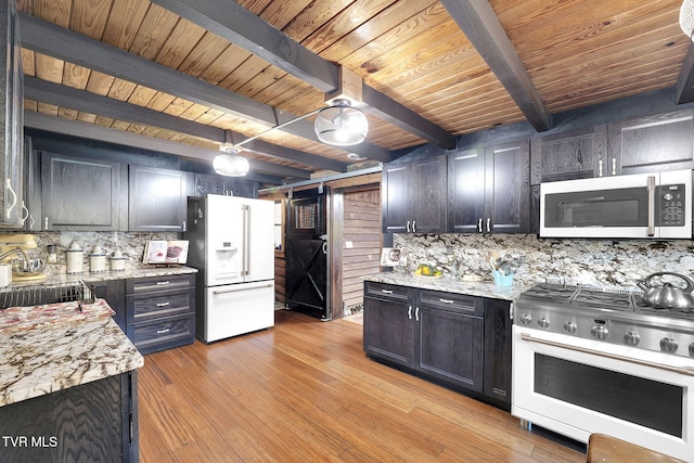 kitchen featuring light stone counters, high end stainless steel range oven, white refrigerator with ice dispenser, beam ceiling, and a barn door