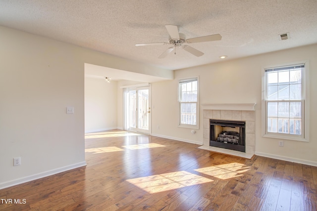 unfurnished living room featuring ceiling fan, a fireplace, a healthy amount of sunlight, and wood-type flooring