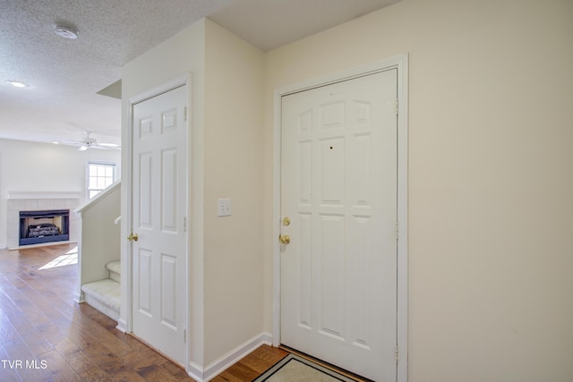 foyer entrance with a fireplace, hardwood / wood-style floors, a textured ceiling, and ceiling fan