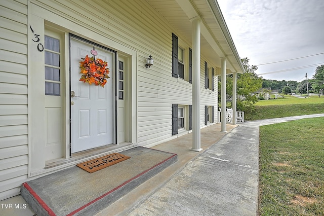 view of exterior entry with a yard and a porch