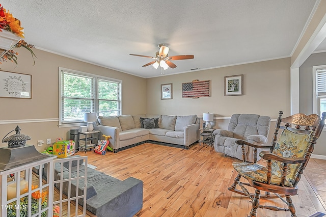 living room with ceiling fan, light hardwood / wood-style floors, ornamental molding, and a textured ceiling