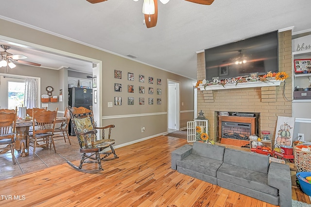 living room with ceiling fan, light wood-type flooring, ornamental molding, and a brick fireplace