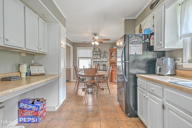 kitchen featuring ceiling fan, light tile patterned flooring, black refrigerator, white cabinets, and ornamental molding