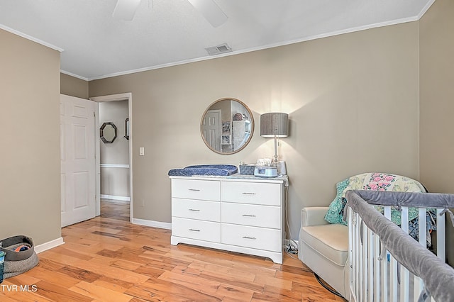 unfurnished bedroom with a crib, light hardwood / wood-style flooring, ceiling fan, and crown molding