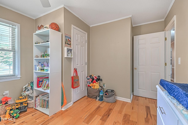 recreation room featuring crown molding, light hardwood / wood-style flooring, ceiling fan, and a healthy amount of sunlight