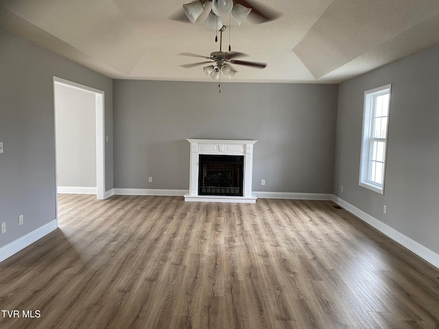 unfurnished living room featuring ceiling fan, light hardwood / wood-style floors, and a tray ceiling