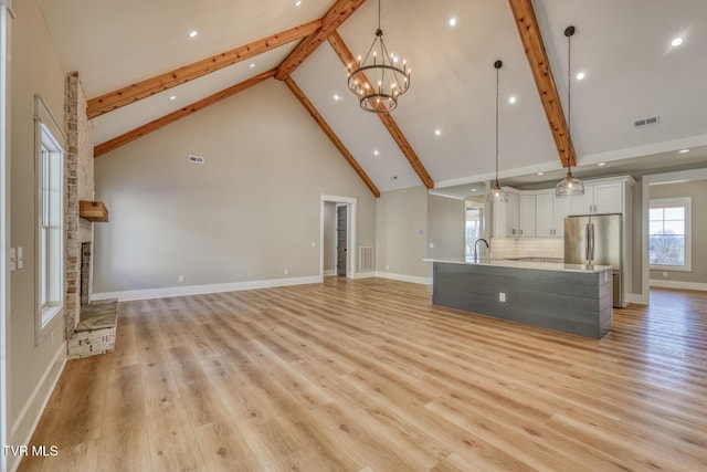 unfurnished living room with high vaulted ceiling, light wood-type flooring, beam ceiling, and an inviting chandelier