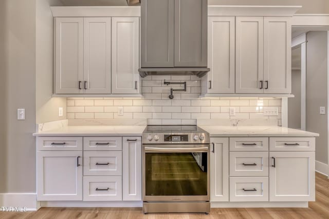 kitchen with light hardwood / wood-style floors, stainless steel electric range, decorative backsplash, white cabinets, and light stone counters