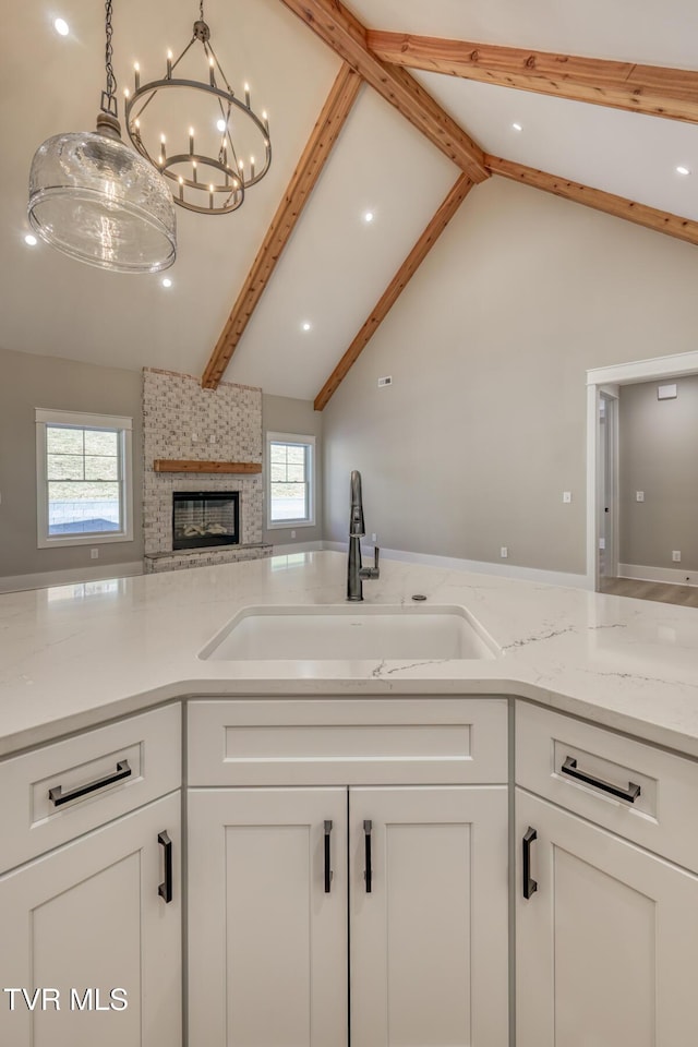 kitchen with white cabinets, vaulted ceiling with beams, a fireplace, and sink