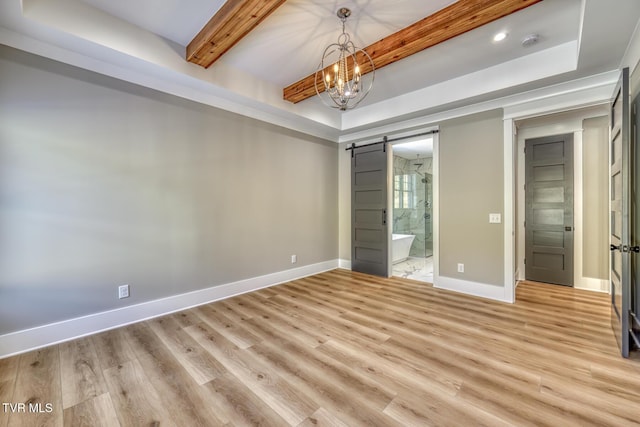 unfurnished bedroom featuring a barn door, a tray ceiling, light wood-type flooring, connected bathroom, and a chandelier