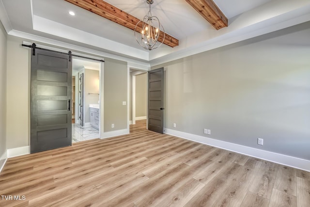 unfurnished bedroom with ensuite bathroom, a barn door, a notable chandelier, beam ceiling, and light hardwood / wood-style flooring