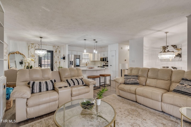 living room with a notable chandelier, light hardwood / wood-style floors, sink, and a textured ceiling